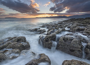 flow of water on gray rocks under white clouds and blue sky during daytime, penmon, anglesey