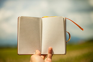 selective focus photography of person holding black-lined graphing notebook