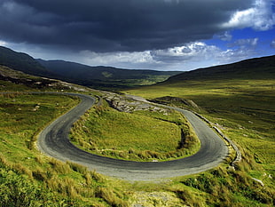 brown asphalt road near mountain under dark skies