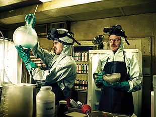 two men wearing gas mask and gray jumpsuits with black aprons