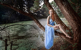 woman in blue spaghetti strap dress sitting on brown branch