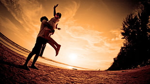 low-angle photography of man standing near shore carrying woman raising hands on air
