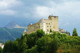 white castle on top of hill beside trees under cloudy sky during daytime