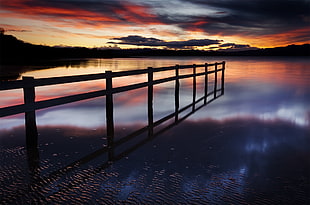 wooden fence in body of water under dark sky photograph
