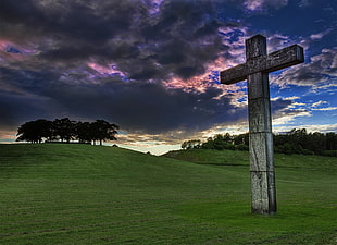 stock photography of gray wooden cross on grass field under cloudy sky