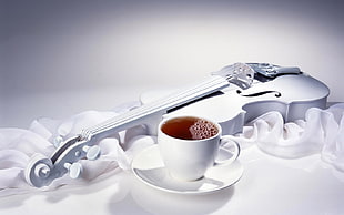 white ceramic tea cup with saucer beside white wooden violin