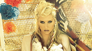 woman with blonde braided hair wearing white top leaning on a wicker wall