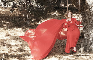 woman red long-sleeved dress sitting on swing during daytime