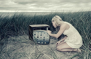 depth of field photography of woman in white tank dress kneeling while opening CRT television