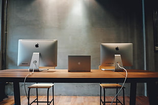 silver MacBook in middle on two iMac on brown wooden desk