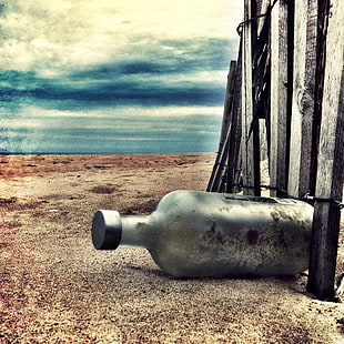 gray bottle beside a fence on sand