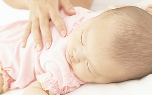 newborn baby wearing pink clothes while laying down on bed