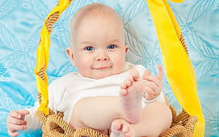 baby wearing white onesie sitting on basket