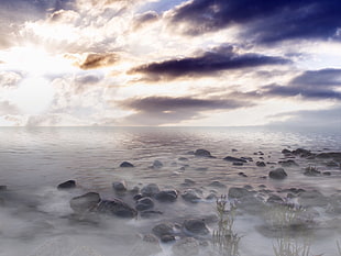 beach with stones covered with fogs under white clouds blue sky