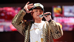 man wearing gold-colored and black coat and white cap holding microphone