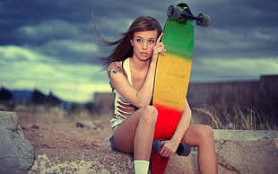 woman wearing white tank top holding red, yellow, and green pintail long board