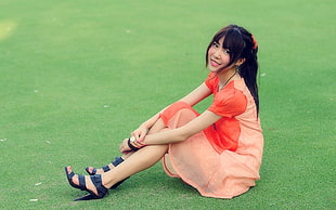 woman wearing orange dress sitting on green grass field