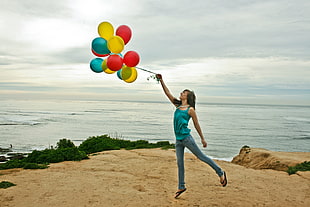 woman with blue tank top carrying a balloon near sea under blue sky