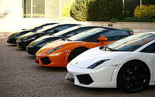 three black super car next to orange Lamborghini Aventador beside white Lamborghini Aventador