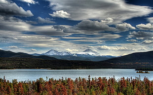 body of water near mountain under white and gray clouds during daytime