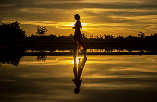 silhouette of woman walking beside water with reflection