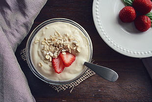 bowl of yogurt with flakes and sliced strawberries placed on brown wooden table