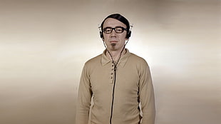 man in brown collared long-sleeve shirt with corded headphone and black framed eyeglasses standing with brown background HD wallpaper
