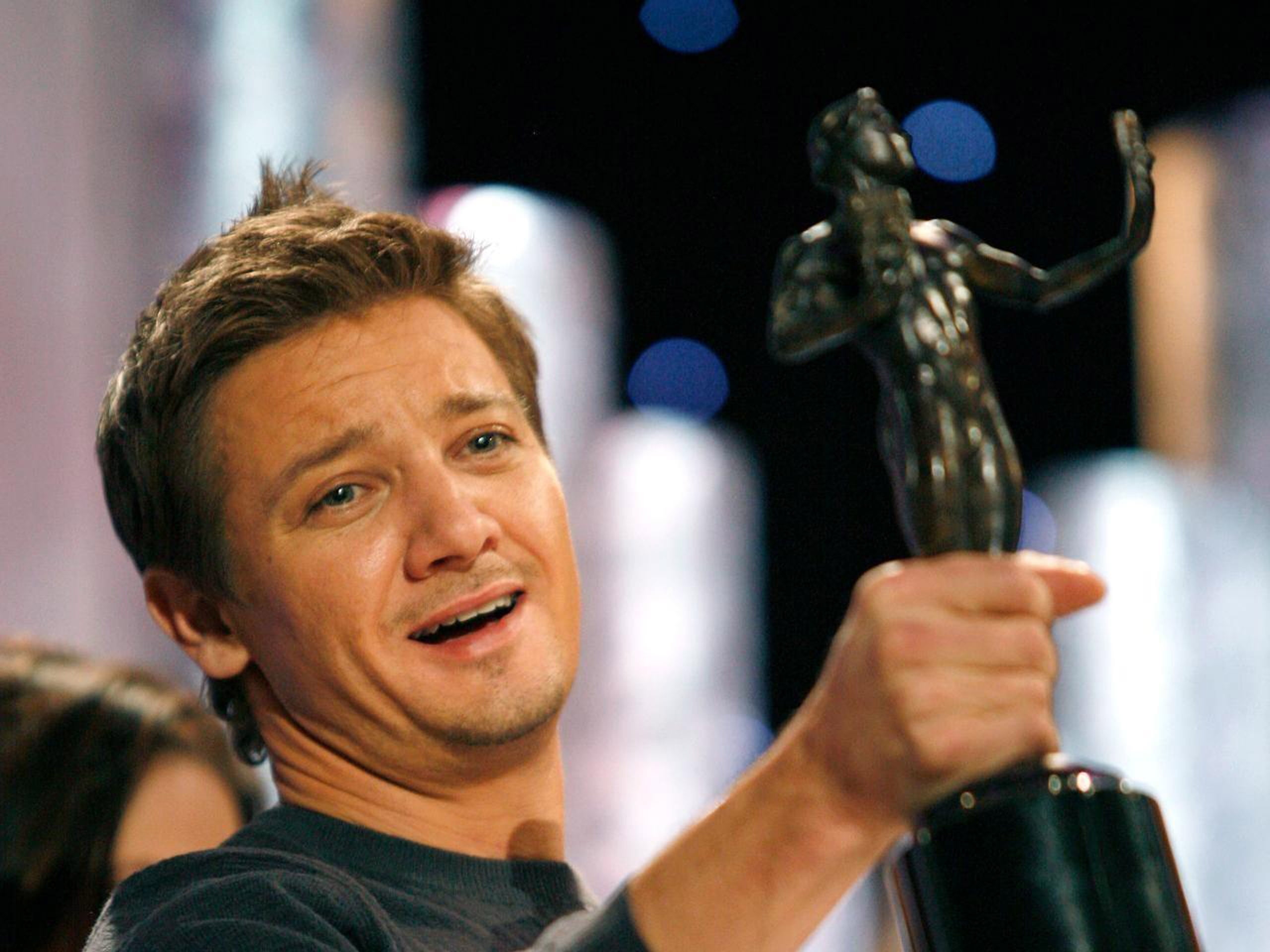 Jeremy Renner holding award trophy