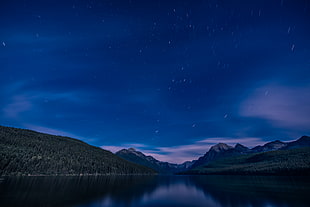 calm water between two mountains under the blue starry night, bowman lake, montana HD wallpaper