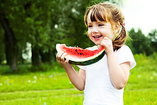 girl holding sliced of watermelon during daytime