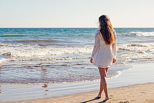woman wearing white long-sleeved dress standing near seashore on white sand during golden hour