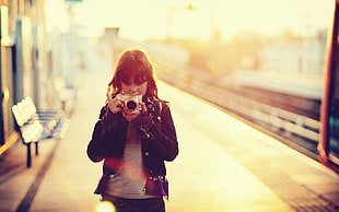 woman holding camera near train rails during sunset