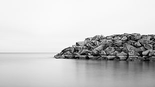 grayscale photo of grey rocks beside calm body of water