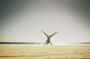 man in beige long-sleeved shirt and pants hand stand on sand during daytime