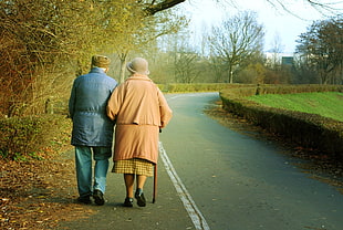 man and woman walking on concrete pavement in between trees