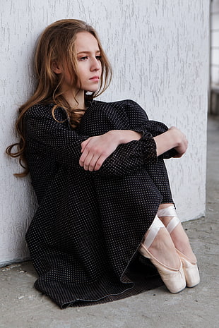 woman in dotted dress wearing ballerina shoes sitting near wall