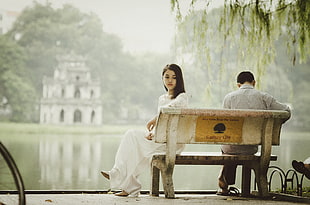 couple sitting on a white bench with a space between in front on a body of water