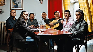 group of man sitting on a table with man holding guitar