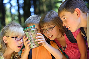boy wearing orange t-shirt holding glass jar beside two girl and one boy