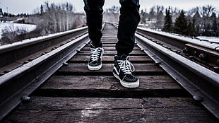 person wearing black-and-white Vans low-top sneakers walking on brown railways