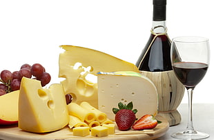 white slice cheese,red grapes,strawberries,black wine bottle and clear wine glass filled with wine