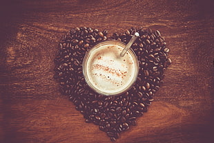 white cup surrounded by beans forming heart on brown wooden surface
