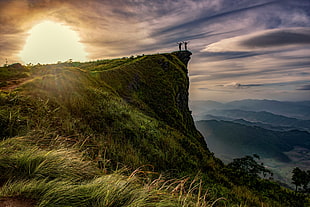couple standing on the cliff of the mountain during daytime HD wallpaper