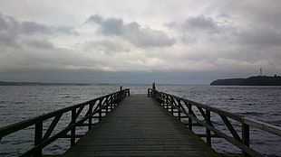 person taking photo of gray wooden dock under gray clouds