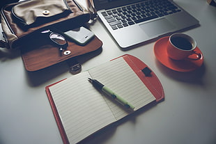 photo of orange ceramic cup and saucer near gray laptop computer on white table