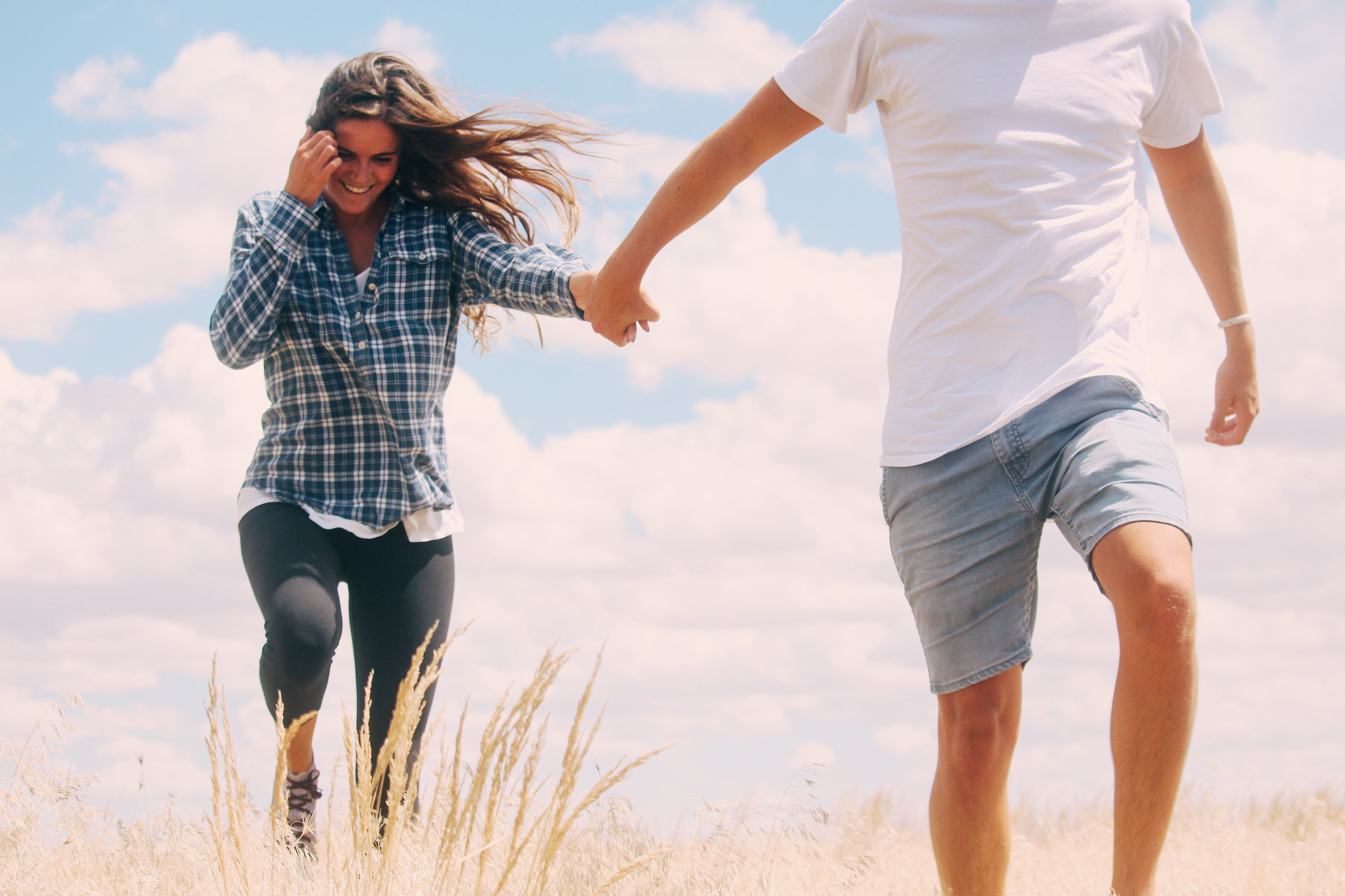 man and woman holding hands on yellow grassy field during daytime