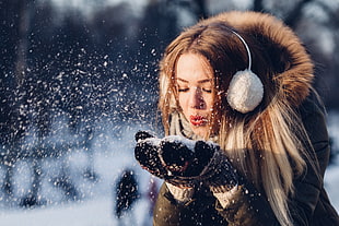 woman wearing coat and earmuffs blowing snow