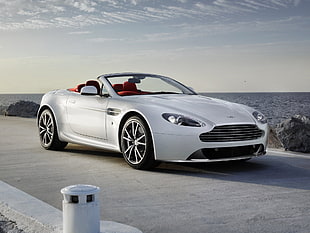 photo of gray convertible coup on roadway beside sea