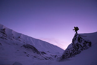 low angle photo of man wearing backpack holding ski poles near snow-caped cliff