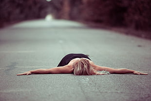 woman in black dress lying on concrete road during daytime
